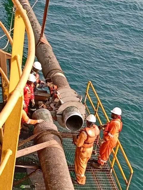 Crew in PPE working a large pipe joint over the water