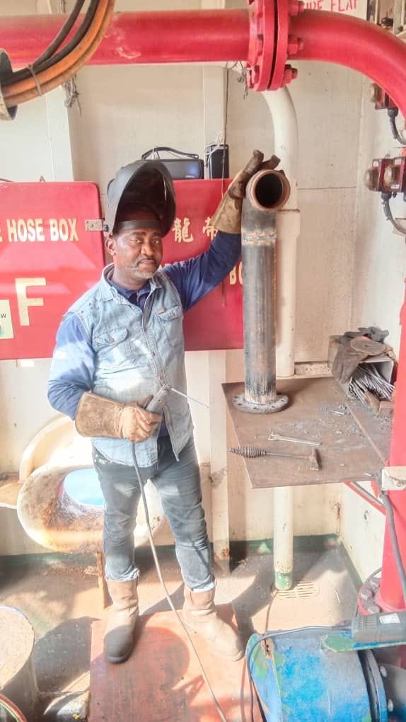 Welder with helmet raised beside red fire-suppression pipework